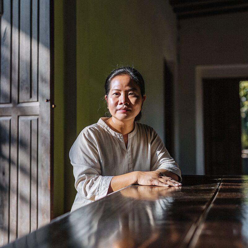 a Vietnamese woman in her mid fifties seated at a wooden table in warm afternoon light