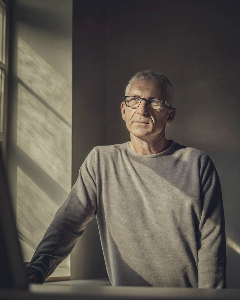 a white man in his late forties at a standing desk by a window at dusk