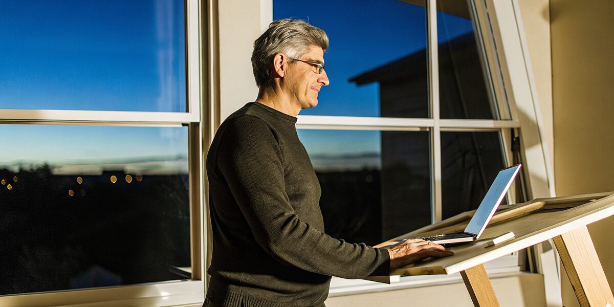 a white man in his late forties at a standing desk by a window at dusk