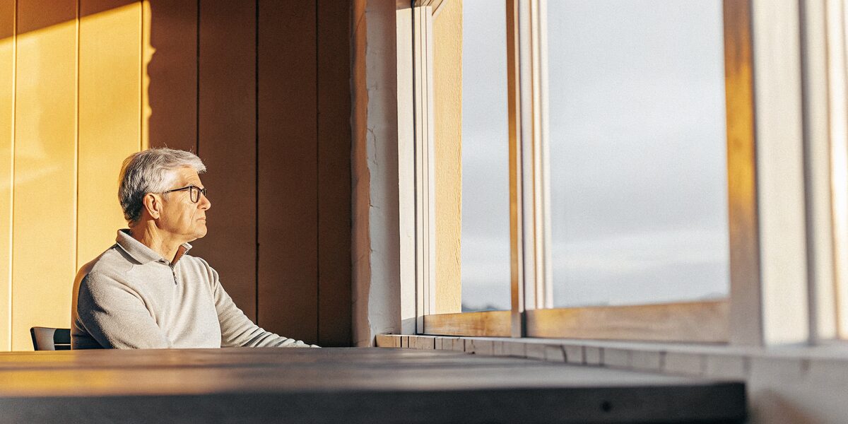 a white man in his mid sixties seated in a quiet room in warm early light